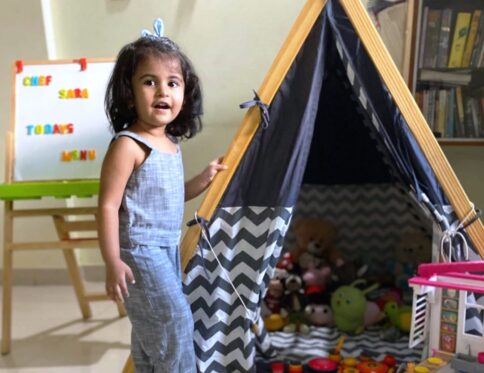 A small girl standing in front of her A-Shape kids tent in grey color